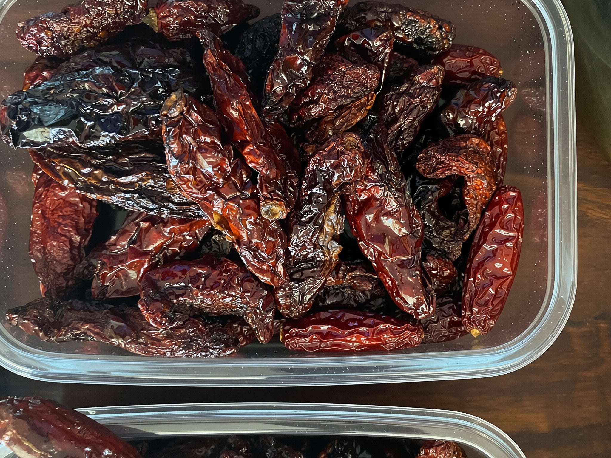 Dried red morita chilies in a clear plastic container on a wooden surface