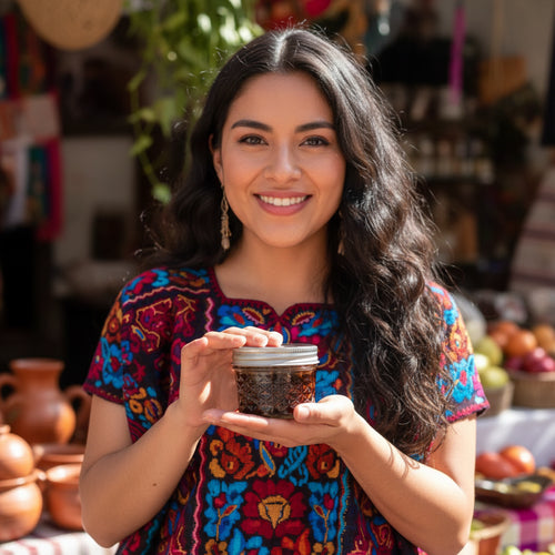 Mexican woman in colorful traditional clothing holding a jar of Chili Flores, surrounded by rustic decor